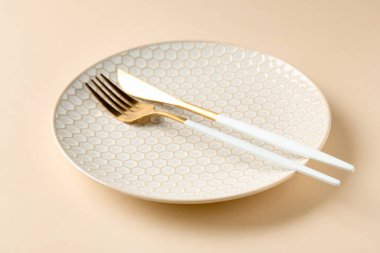 Bej arka planda seramik tabak ve çatal bıçak takımı, yakın plan.