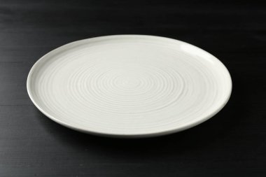 Empty ceramic plate on black wooden table, closeup
