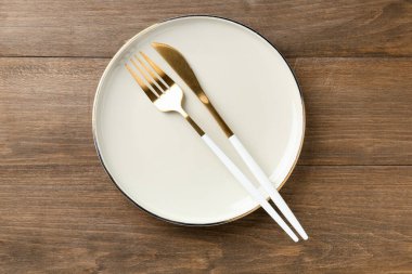 Clean ceramic plate and cutlery on wooden table, top view