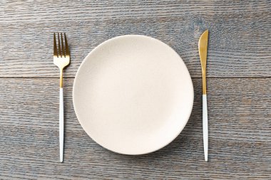 Clean ceramic plate and cutlery on wooden table, top view