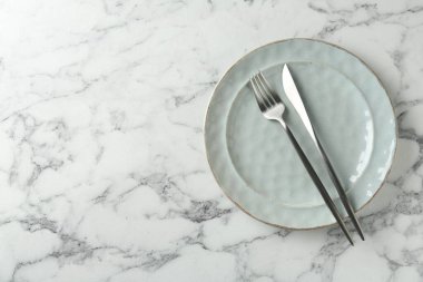 Ceramic plate and cutlery on white marble table, top view. Space for text