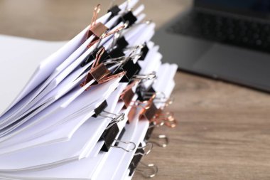 Many documents with binder clips and laptop on wooden desk, closeup