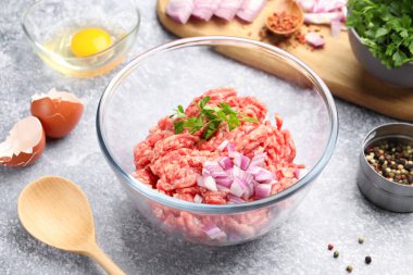 Raw minced meat with onion, parsley, spices and egg on grey table, closeup