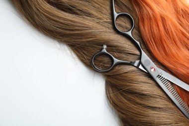 Farklı renklerde güzel saç telleri ve beyaz arka planda makas, üst manzara. Metin için boşluk