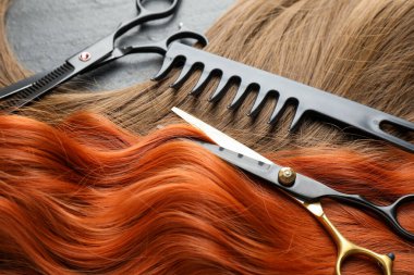 Farklı renklerde güzel saç telleri ve gri arka planda kuaför aletleri, yakın plan.