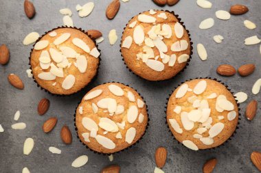 Tasty muffins with almond flakes and nuts on grey table, flat lay