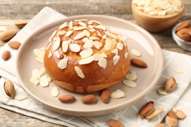 Tasty roll bun with almond flakes and nuts on wooden table, closeup