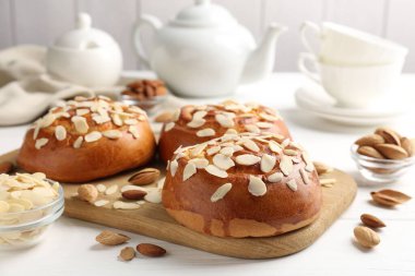 Tasty roll buns with almond flakes, nuts and tea set on white wooden table, closeup
