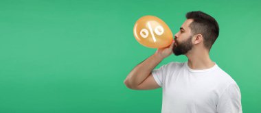 Yeşil arka planda yüzde işareti olan turuncu balon şişiren adam. İndirim teklifi