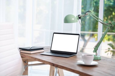 Boş beyaz ekranlı dizüstü bilgisayar, odada lamba ve kırtasiye malzemesi. Rahat ev işyeri