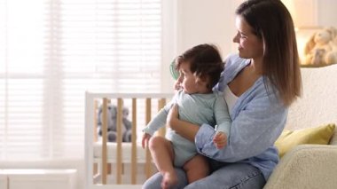 Anne bebeğinin saçını evde koltukta tarıyor.