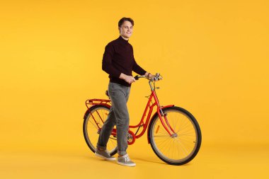 Turuncu arka planda kırmızı bisikletli yakışıklı bir adam.