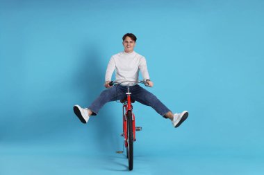 Açık mavi arka planda kırmızı bisiklete binen yakışıklı adam