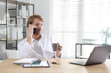 İçkili bir adam ahşap masada akıllı telefondan konuşuyor.