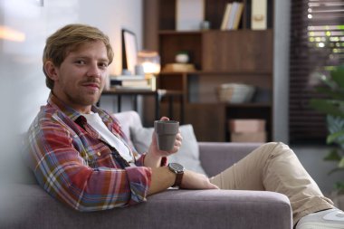 Evdeki kanepede bir bardak içen adam.