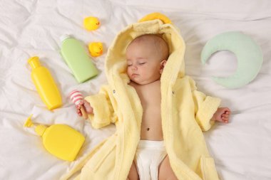 Yataktaki banyo aksesuarları ve bornozlu tatlı bir bebek.