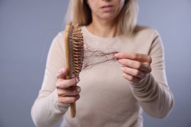 Alopecia sorunu. Kayıp saçlarını gri arka plandaki fırçadan alan kadın, yakın plan