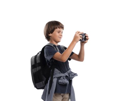 Meslek seçimi. Kameralı ve sırt çantalı küçük çocuk beyaz arka planda fotoğrafçı gibi davranıyor.