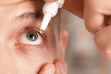 Bulanık arkaplanda göz damlası uygulayan adam, yakın plan