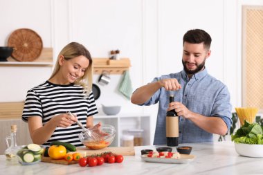 Gülümseyen adam mutfakta karısıyla yemek pişirirken şarap şişesini açıyor.