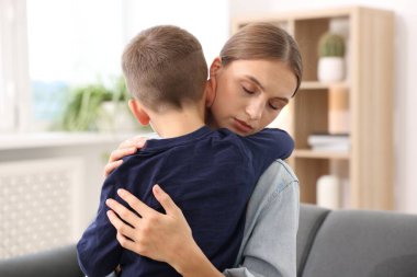 Anne, üzgün oğlunu evde destekleyip kucaklıyor.