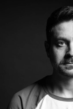 Üzgün adam karanlık arka planda ağlıyor, yakın planda. Siyah ve beyaz etkisi