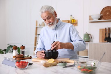 Mutfaktaki beyaz mermer masada yaşlı bir adam yemek pişiriyor.