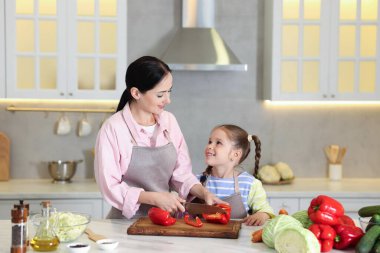 Küçük yardımcı. Anne ve kızı mutfaktaki beyaz mermer masada birlikte yemek pişiriyorlar.