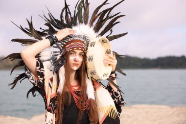 Kızılderili başlıklı güzel bir şaman kadın portresi. Yüzü nehir kenarında boyalı ve tef çalıyor. Metin için boşluk