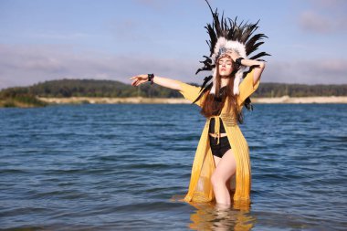 Amerikan yerlisi başlıklı güzel bir şaman kadın nehir suyunda yürürken yüzünü boyuyor. Metin için boşluk