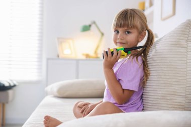 Evdeki koltukta telsizle oynayan küçük bir kız. Mesaj atmak için yer var.