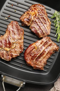 Pan with grilled beef steaks, rosemary and peppercorns on grey table, top view