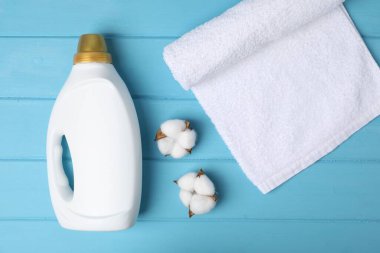 Bottle of fabric softener, towel and cotton flowers on light blue wooden table, flat lay