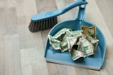 Dollar banknotes, dustpan and broom on floor, closeup