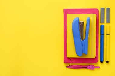 Blue stapler and other stationery on yellow background, flat lay. Space for text
