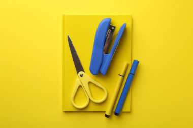 Zımba, makas, defter ve keçeli kalemler sarı arka planda, düz yerde