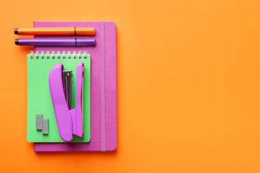 Stapler, metal staples, notebooks and felt pens on orange background, flat lay. Space for text