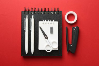 Stapler and other stationery on red background, flat lay