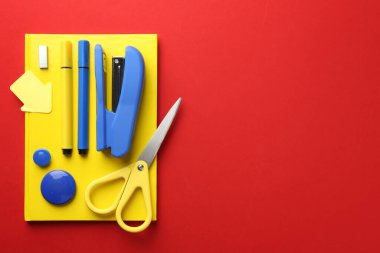 Stapler and other stationery on red background, top view. Space for text