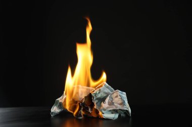 Burning dollar banknotes on black table against dark background