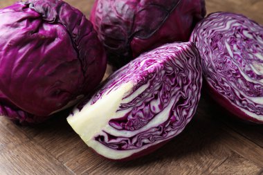 Whole and cut red cabbages on wooden table, closeup