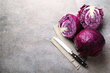 Whole and cut red cabbages with knife on grey table, flat lay. Space for text