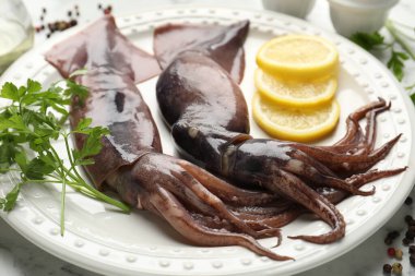 Raw squids, lemon and parsley on white marble table, closeup