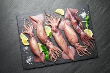 Raw squids, lemon and basil on black table, top view