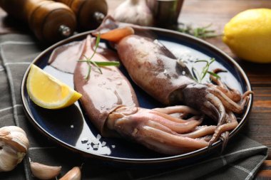 Raw squids, lemon and rosemary on wooden table, closeup