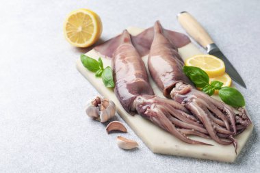 Çiğ mürekkep balıkları, limon, bıçak ve fesleğen açık gri masada, yakın plan. Metin için boşluk