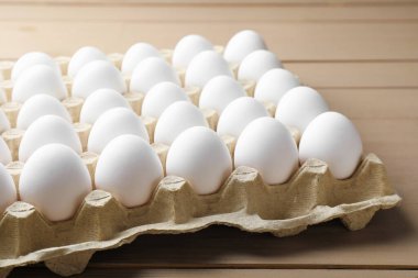 Many raw chicken eggs in carton on wooden table, closeup