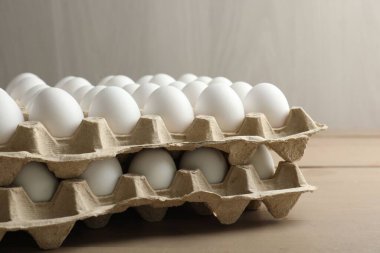 Many raw chicken eggs in cartons on wooden table, closeup