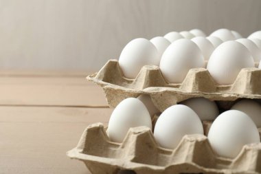 Many raw chicken eggs in cartons on wooden table, closeup. Space for text