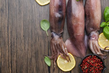 Raw squids, lemon slices, spices and basil on wooden table, flat lay. Space for text